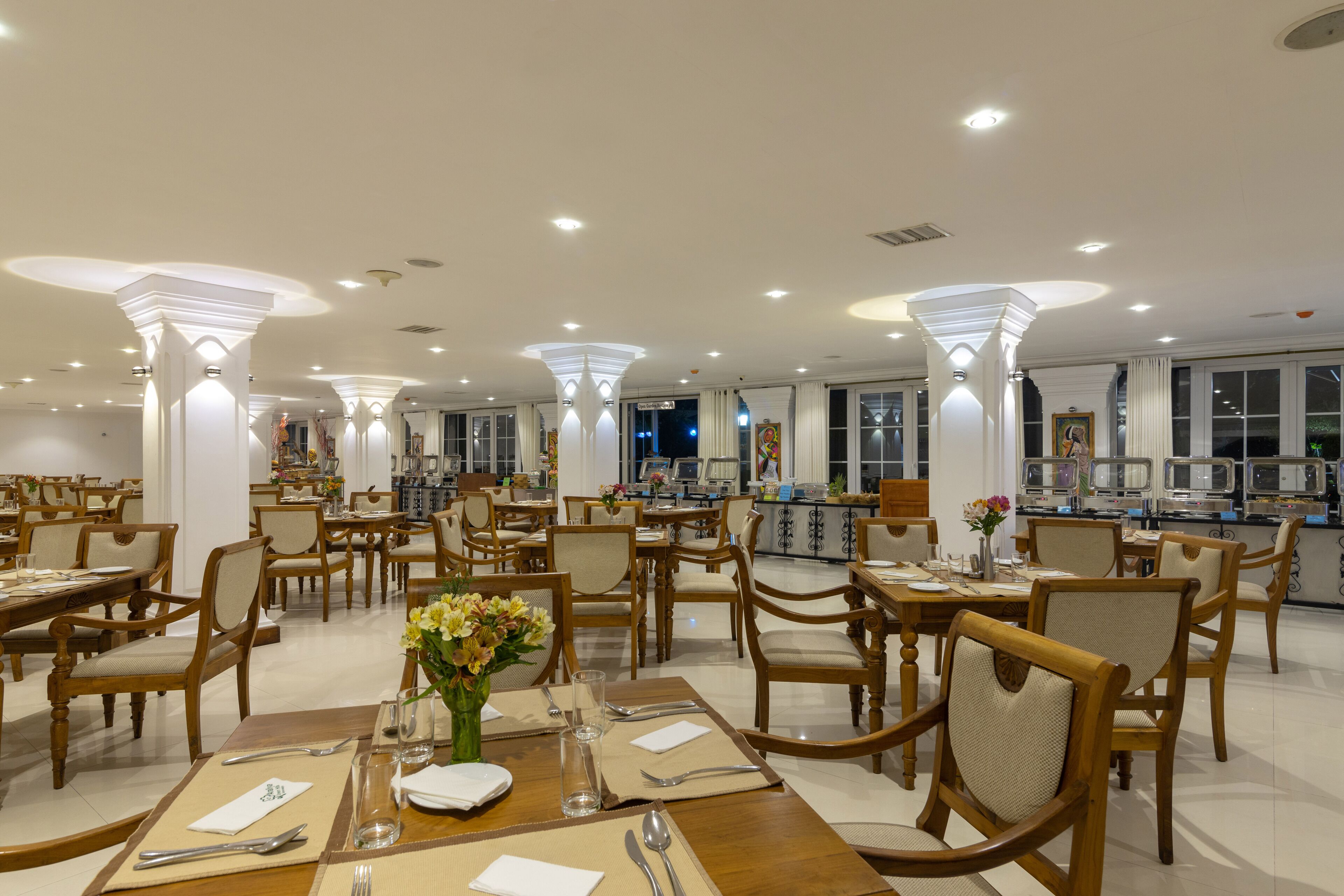 A spacious dining area with multiple tables and chairs, featuring a modern chandelier and large windows.