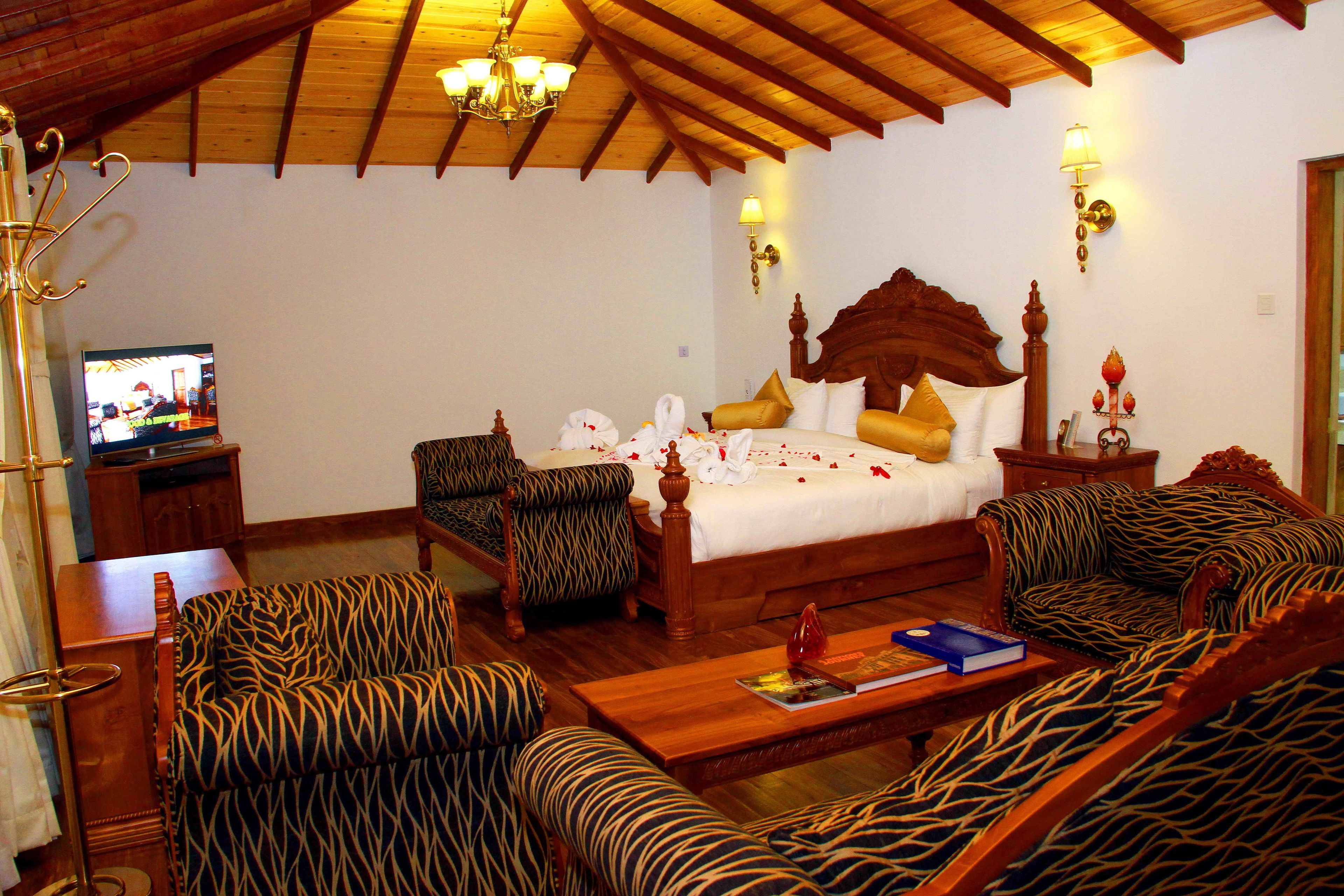A hotel room with a large bed, zebra-patterned sofas, a wooden coffee table, and a television on a stand.