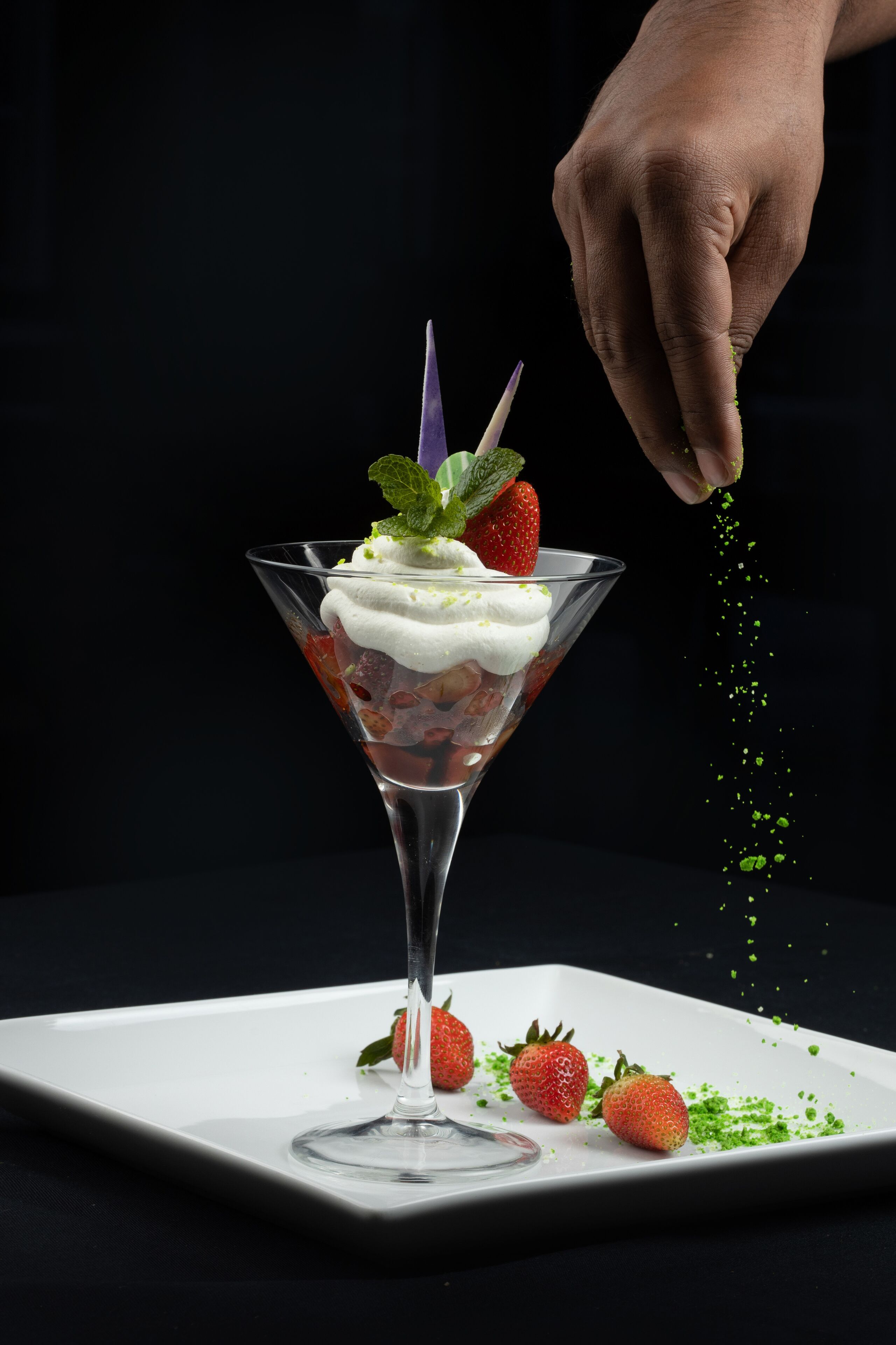 Postre en copa de martini con fresas y crema batida, adornado con menta, sobre un plato blanco.