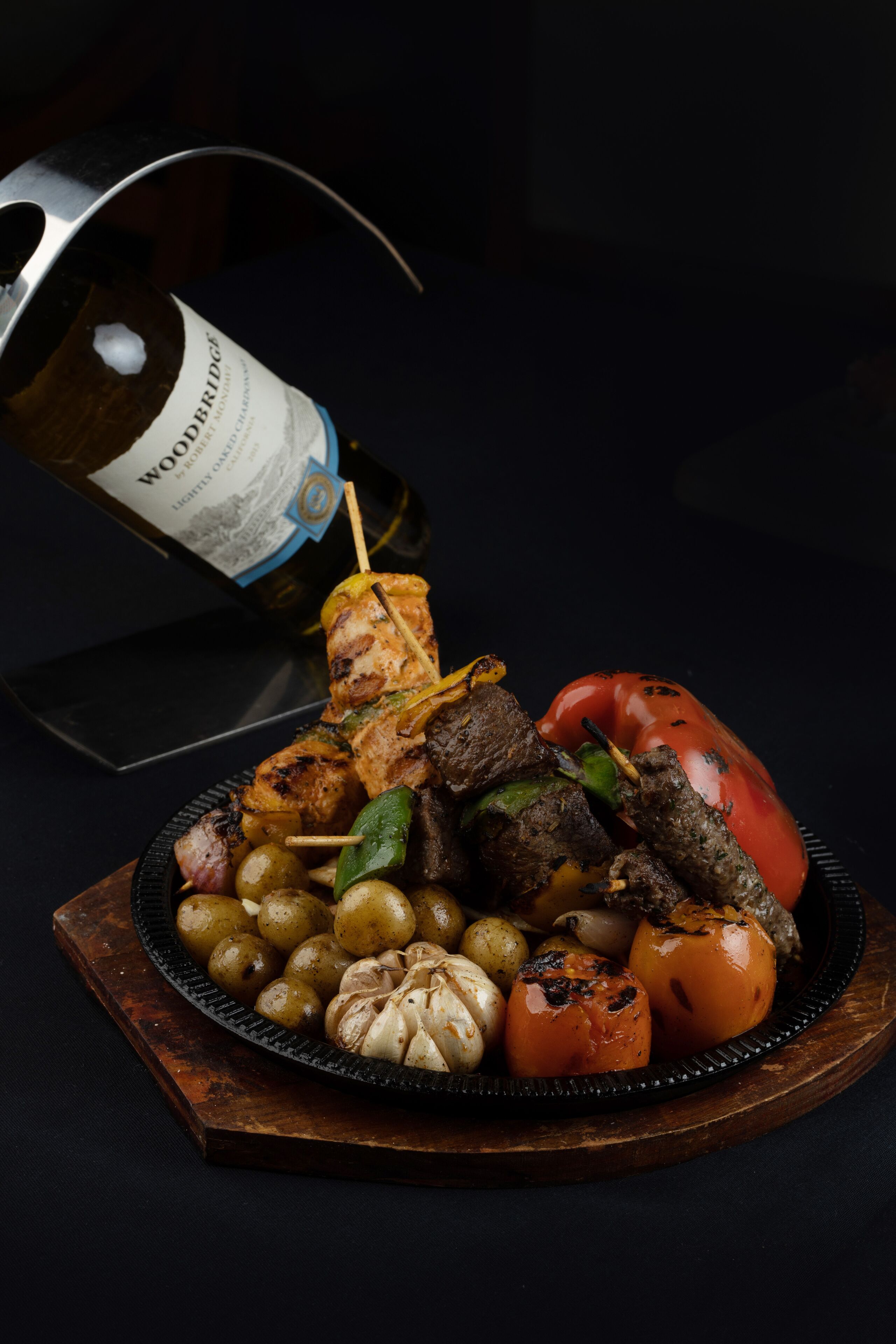 Una tabla de quesos y embutidos con vegetales y una botella de vino.
