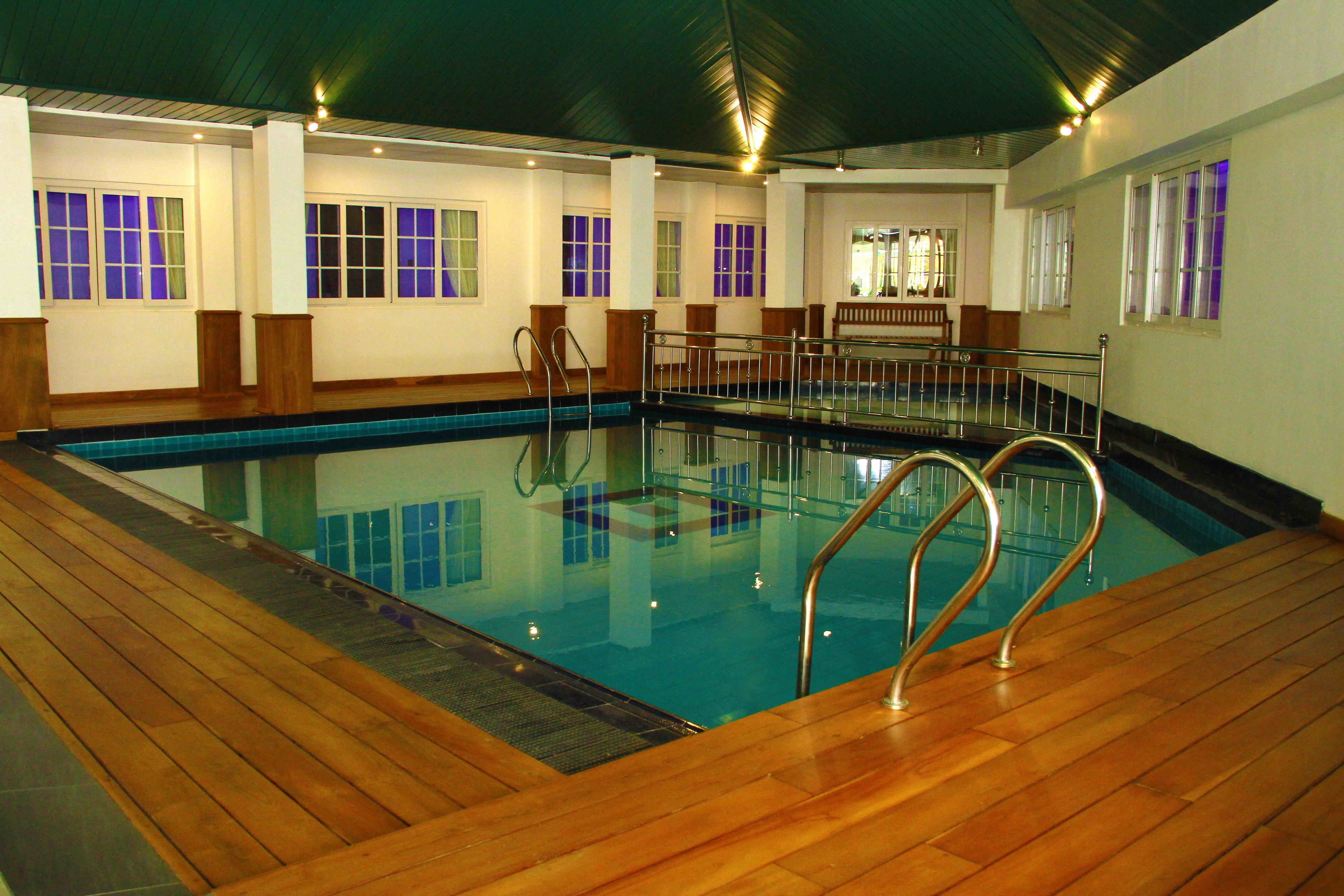 An indoor swimming pool with wooden deck and metal railings.