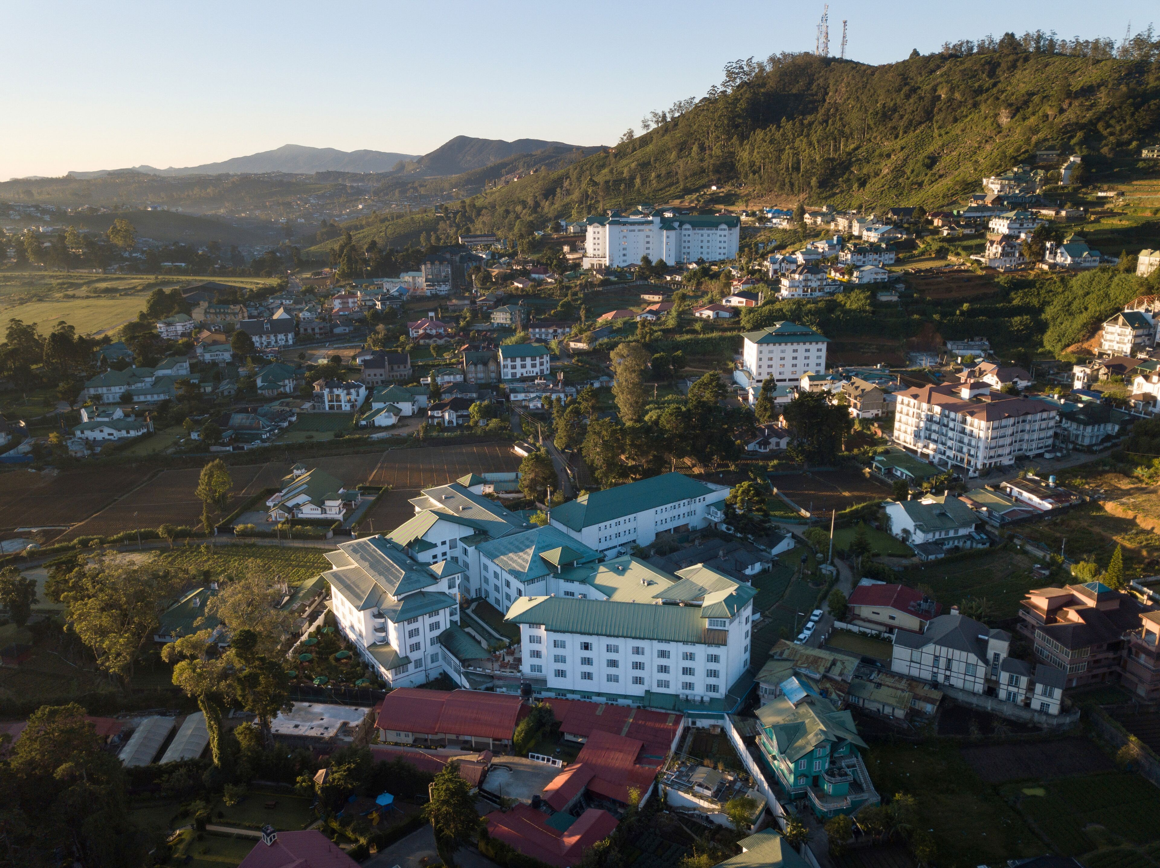An aerial view of a town with a prominent white building with a green roof, surrounded by smaller houses and greenery.