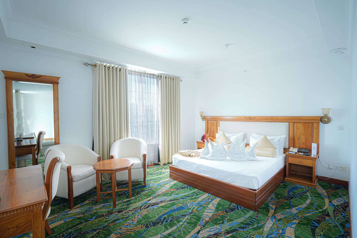 Ein Hotelzimmer mit Bett, Sessel, Tisch, Nachttisch und Spiegel.