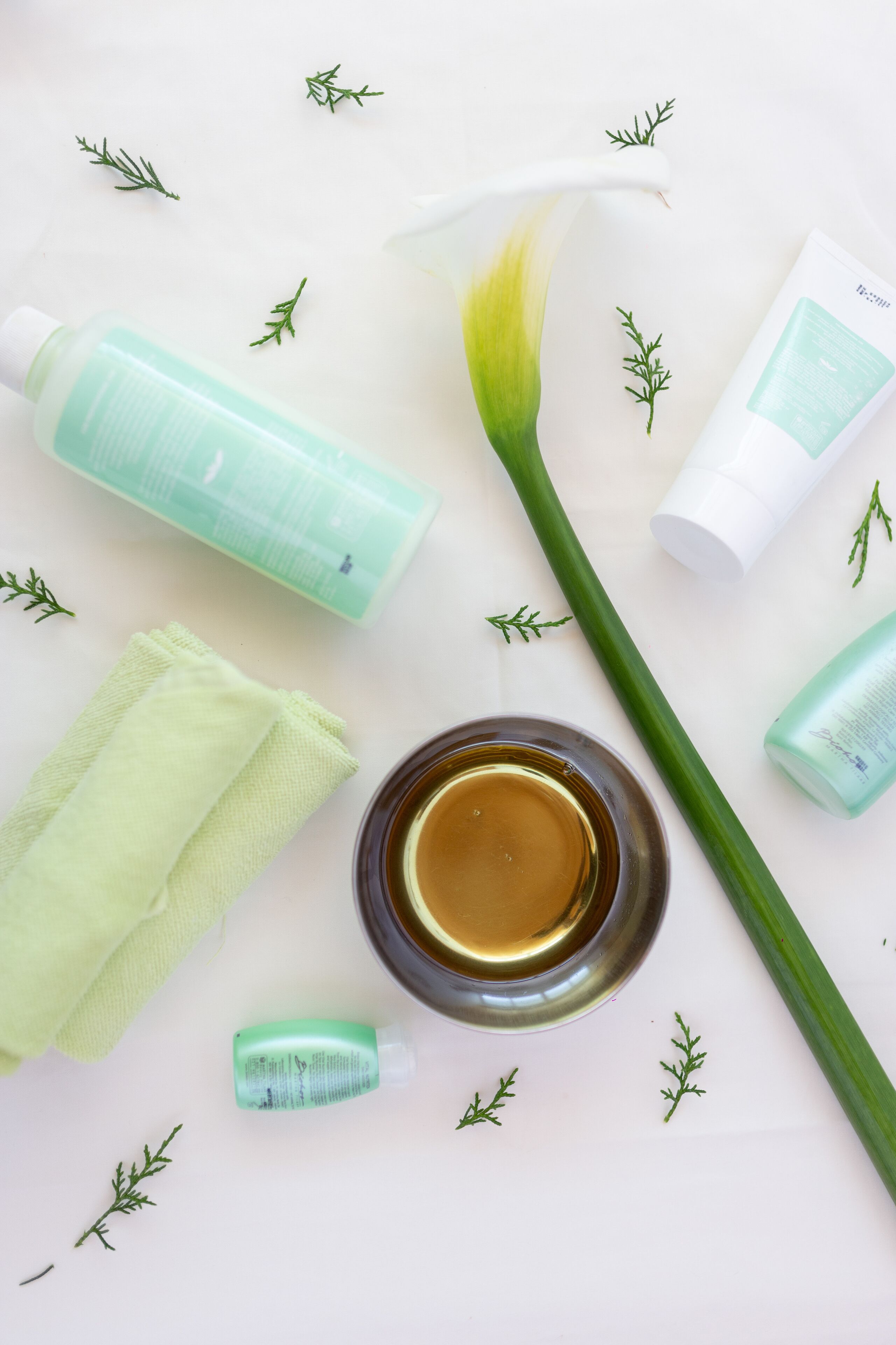 A bathroom with a white countertop, a green towel, a bottle of liquid soap, a green bottle, a white bottle, and a green plant.
