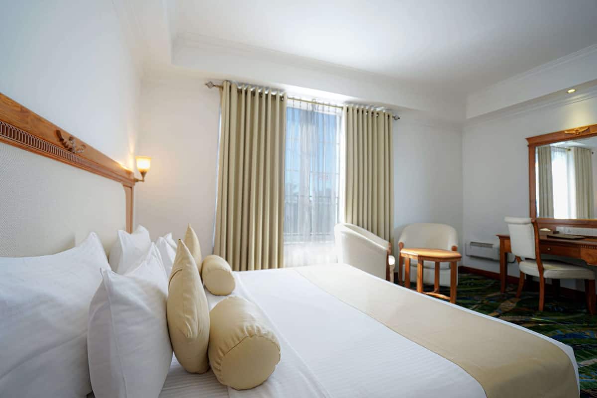 Ein Hotelzimmer mit einem großen Bett, einem Schreibtisch, einem Stuhl und einem Fenster mit Vorhängen.