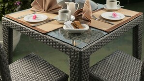 Una mesa con cubierta de vidrio y un frutero escalonado, platos, tazas y cubiertos.