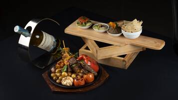 A wooden table with a bottle of wine, a bowl of salad, and a plate of grilled vegetables.
