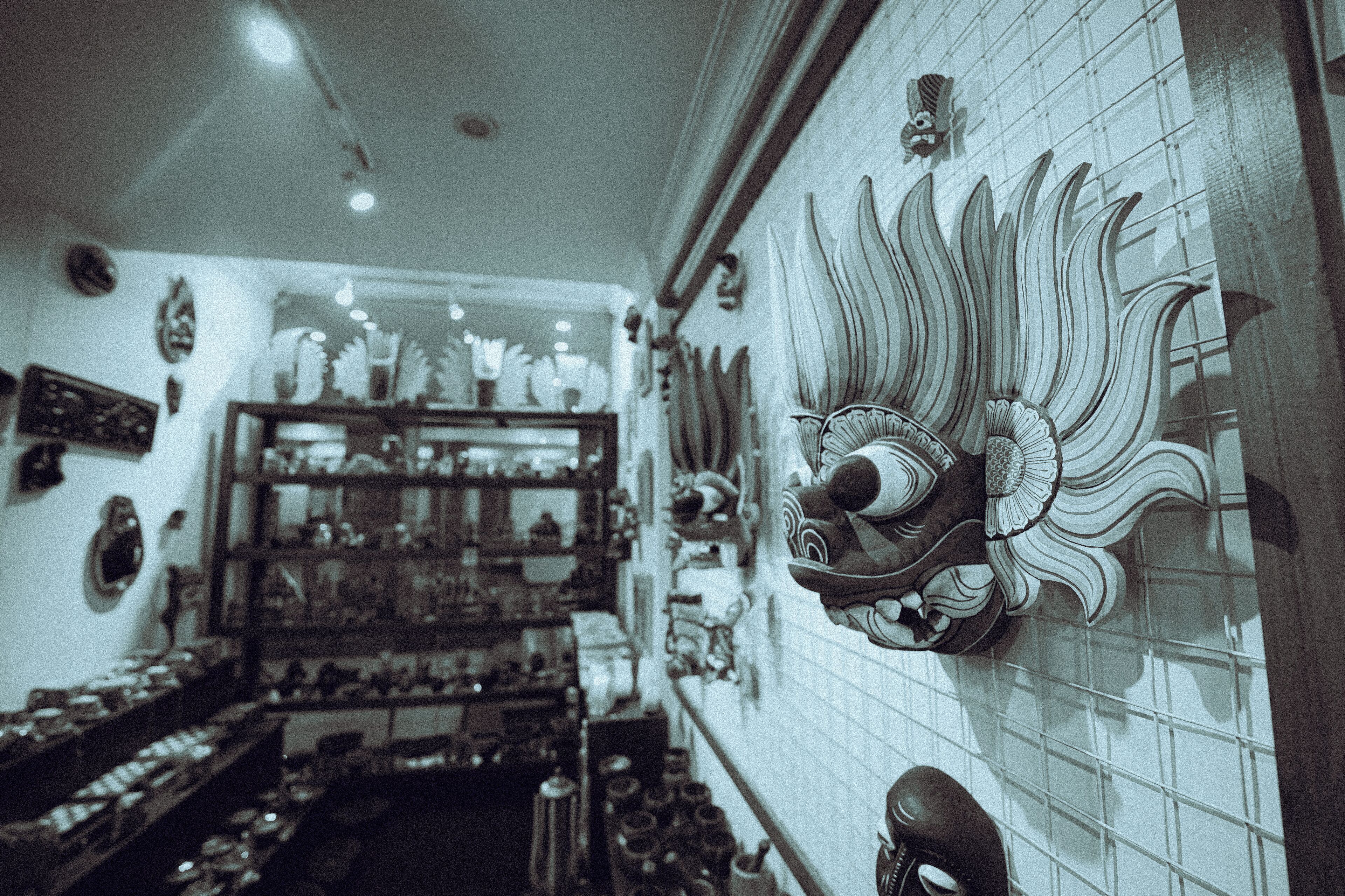 A narrow hallway with shelves displaying various items, a decorative mask on the wall, and a tiled floor.