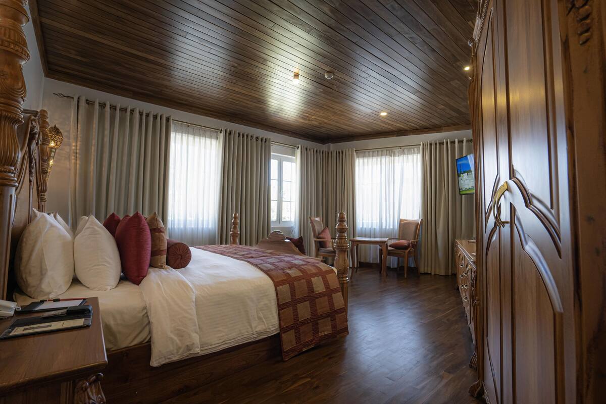 Ein Hotelzimmer mit Holzboden, einem großen Bett mit vielen Kissen, einer hölzernen Kommode und einem Fernseher an der Wand.