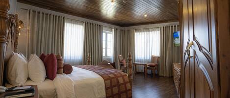 A hotel room with a wooden ceiling, a large bed with multiple pillows, a wooden dresser, and a television on the wall.