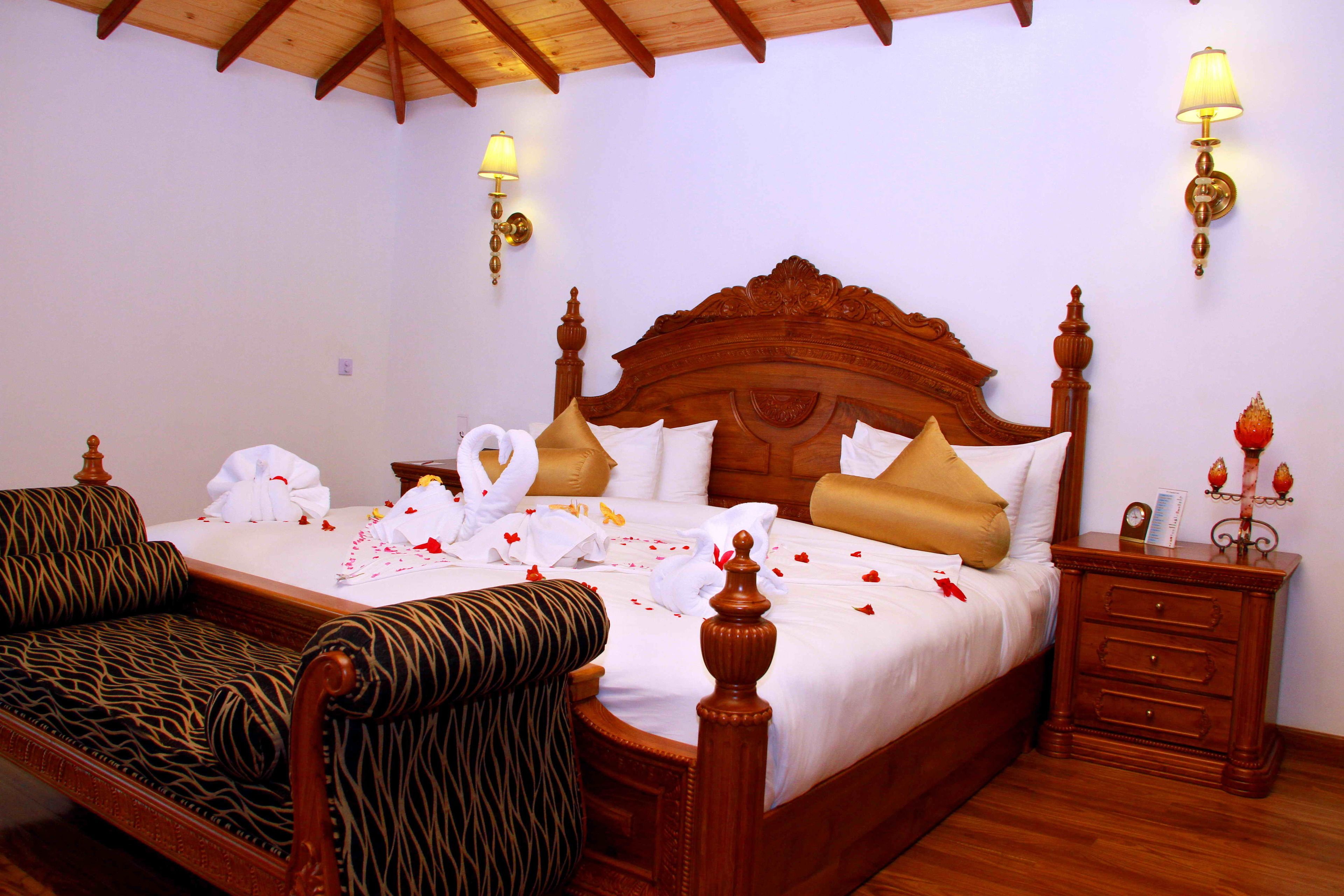 A neatly made bed with a wooden headboard, a bedside table with a lamp, and a patterned sofa.