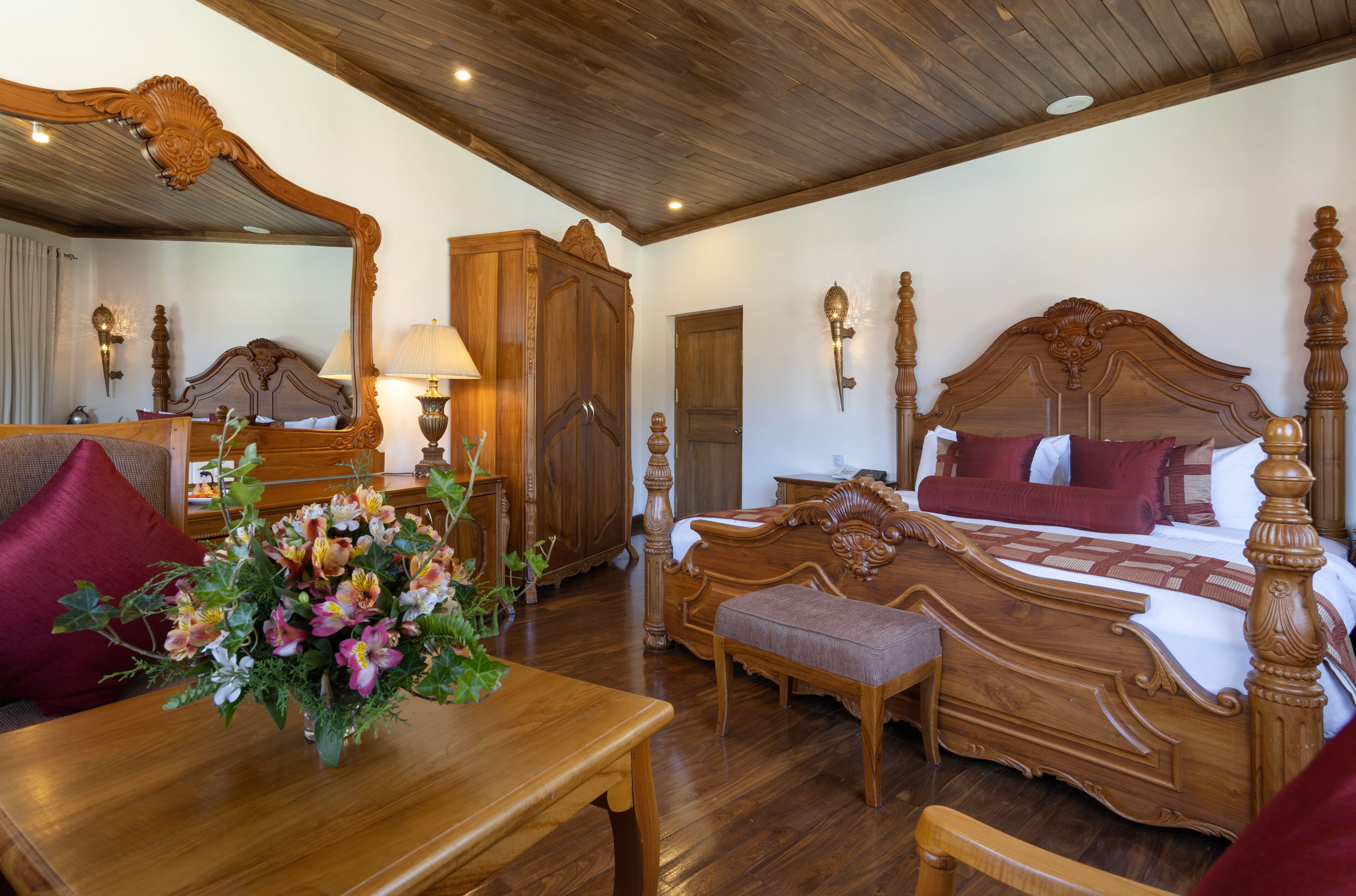 Een slaapkamer met houten vloer, een groot bed, een houten kledingkast, een nachtkastje en een bloemenboeket.