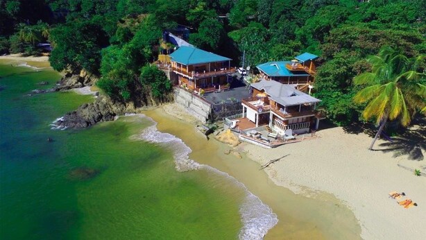 A beachfront property with multiple buildings, including a large structure with a blue roof and several smaller ones. - The Naturalist Beach Resort (Castara)