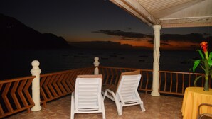 A terrace with two white chairs and a table, overlooking a body of water at sunset. - The Naturalist Beach Resort (Castara)