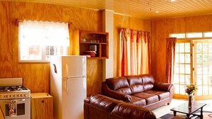 A cozy living room with a brown leather sofa, a white refrigerator, a wooden cabinet, and a window with curtains. - The Naturalist Beach Resort (Castara)