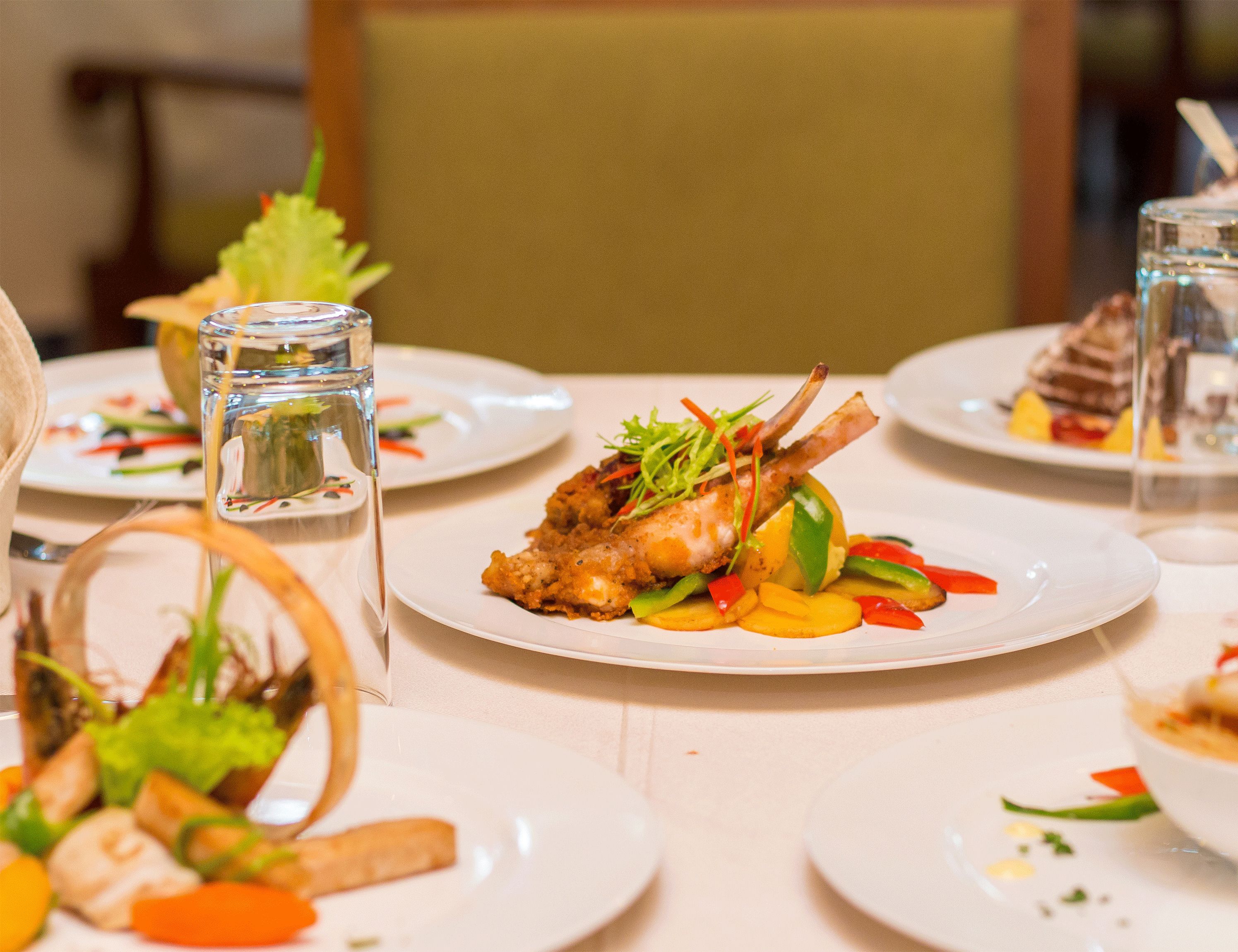 A dining table with plates of food, including a dish with a lamb shank and vegetables.