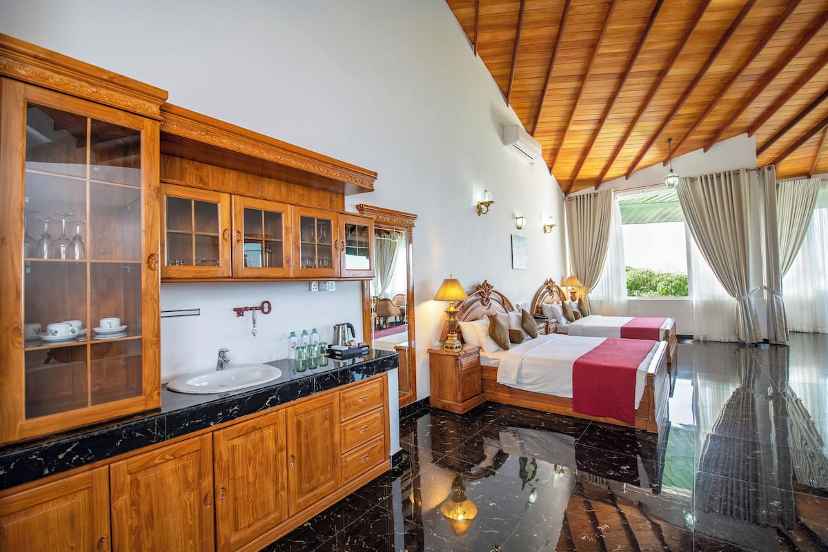 Une chambre d’hôtel avec un meuble en bois doté de portes en verre, un lavabo, un lit recouvert d’une couverture rouge et une table de chevet avec une lampe.