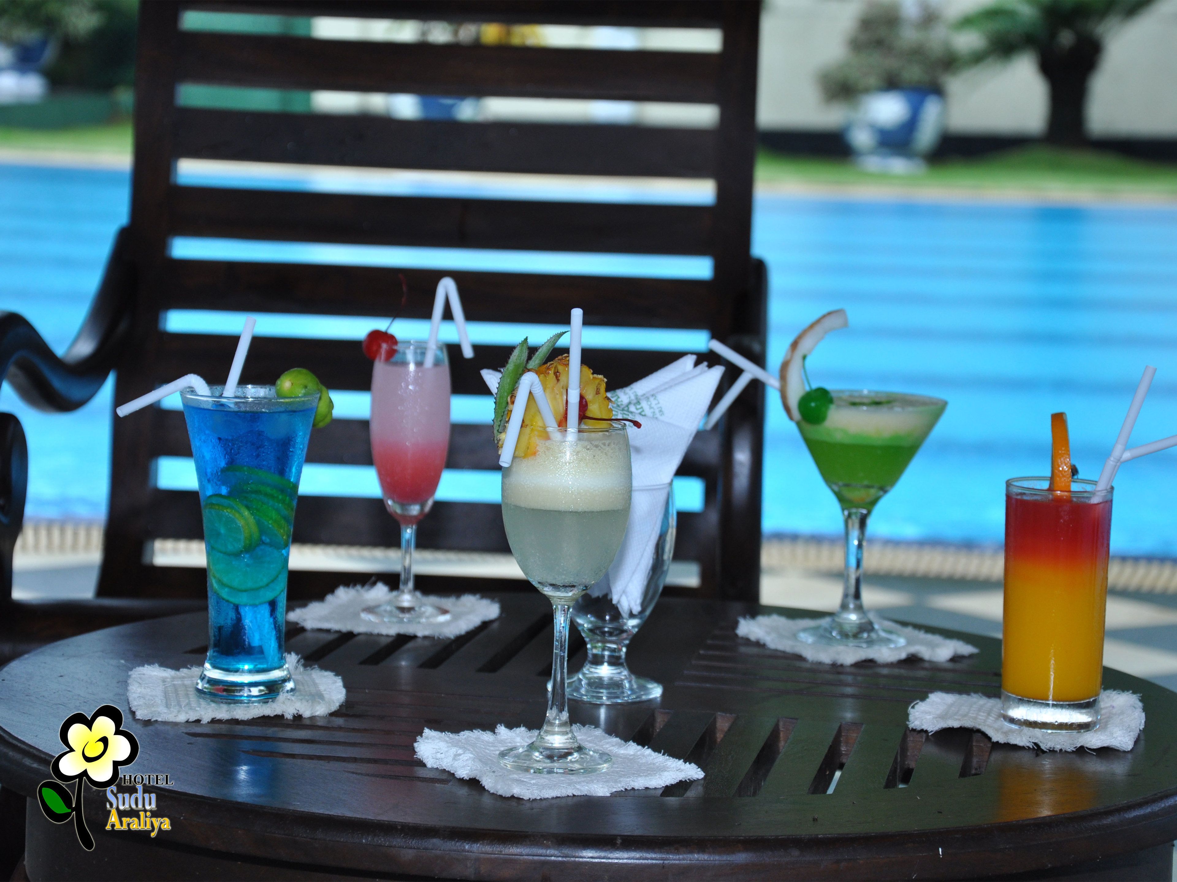A table with four drinks, a logo, and a pool in the background.