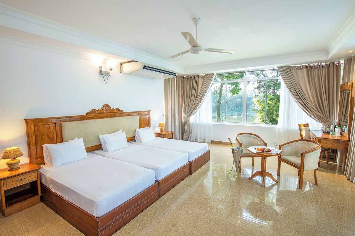 Une chambre d’hôtel avec deux lits, une table à manger, des chaises, un bureau et un ventilateur de plafond.