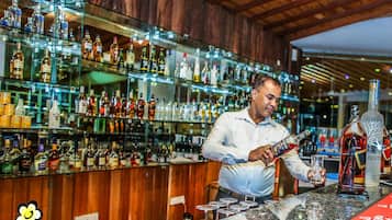 A bar area with shelves of various liquor bottles, a counter with glasses, and a logo for Hotel Sudu Arabiya.
