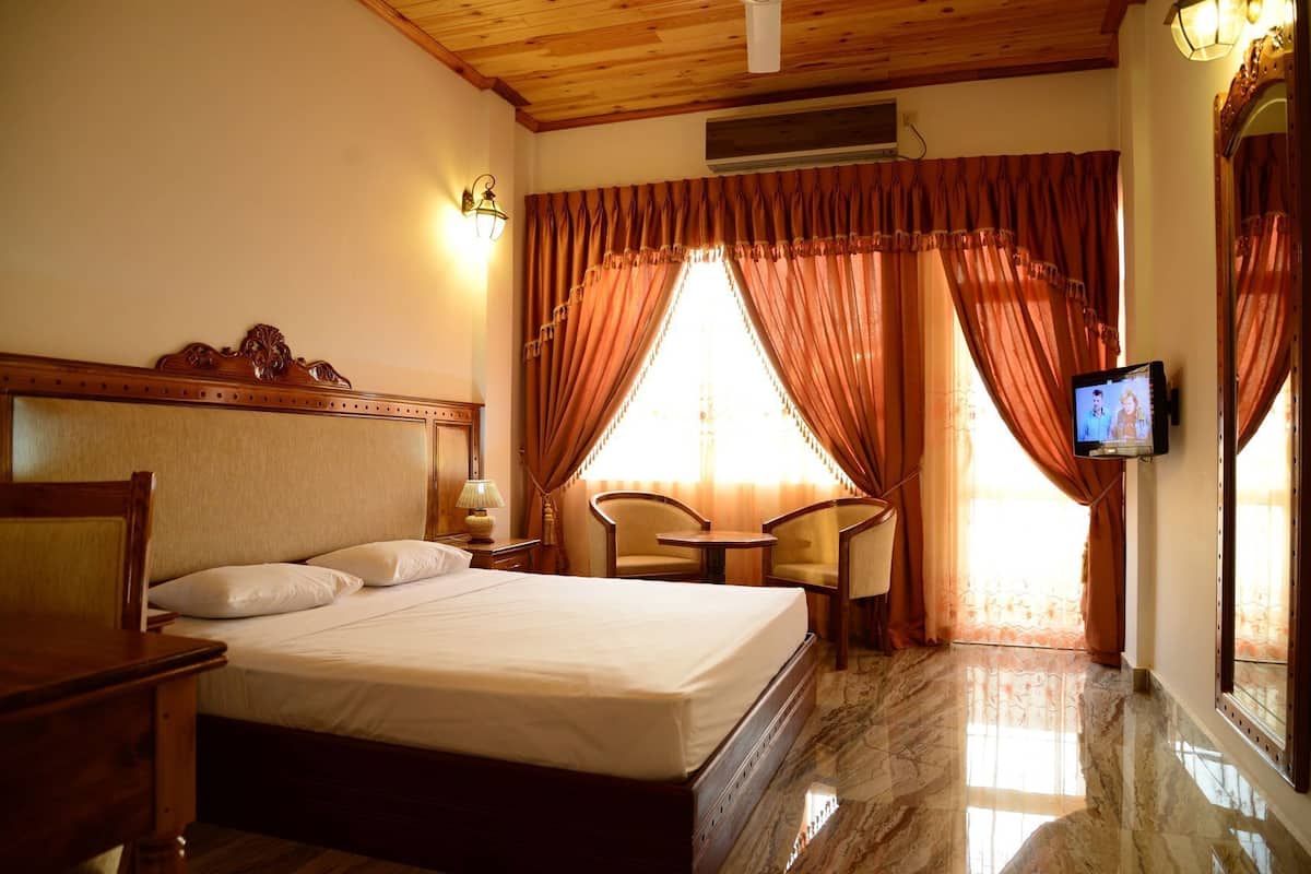 Une chambre d’hôtel avec un lit, une télévision, un bureau, une chaise et une fenêtre avec des rideaux.