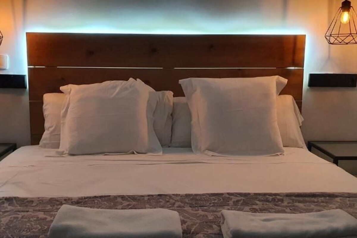 A neatly made bed with white linens and pillows, two bedside tables with lamps, and a headboard with a built-in light.