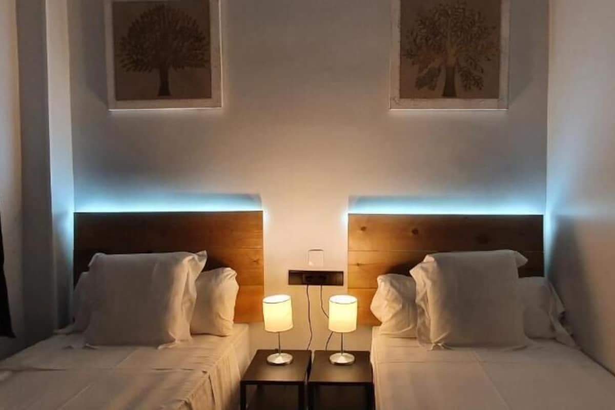 A hotel room with two beds, nightstands, and wall-mounted lamps.