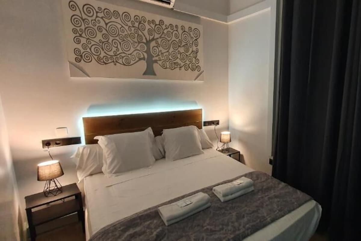 A hotel room with a bed, bedside lamps, a wall art piece, and a curtain.