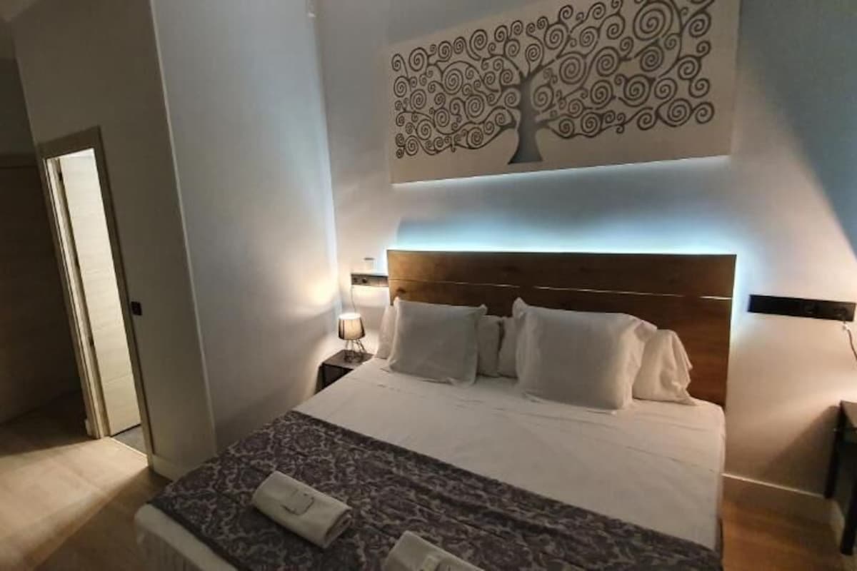 A hotel room with a bed, bedside table, lamp, and a wall-mounted artwork.