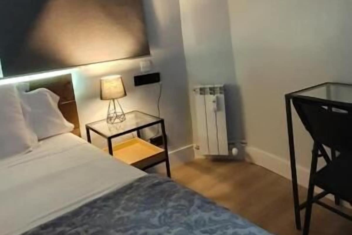 A hotel room with a bed, a desk, a chair, a TV, and a wall-mounted artwork.