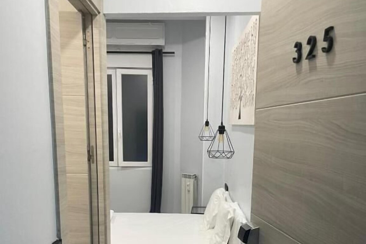 A hotel room with a bed, a bedside table, a wardrobe, and a door leading to another room.