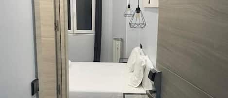 A hotel room with a bed, a bedside table, a wardrobe, and a door leading to another room.