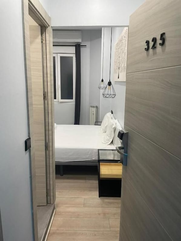 A hotel room with a bed, a bedside table, a wardrobe, and a door leading to another room.