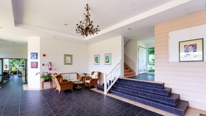 A spacious living area with a staircase, a chandelier, and framed artwork on the walls. - Baan Poolom Beachfront Condominium (Hua Hin)