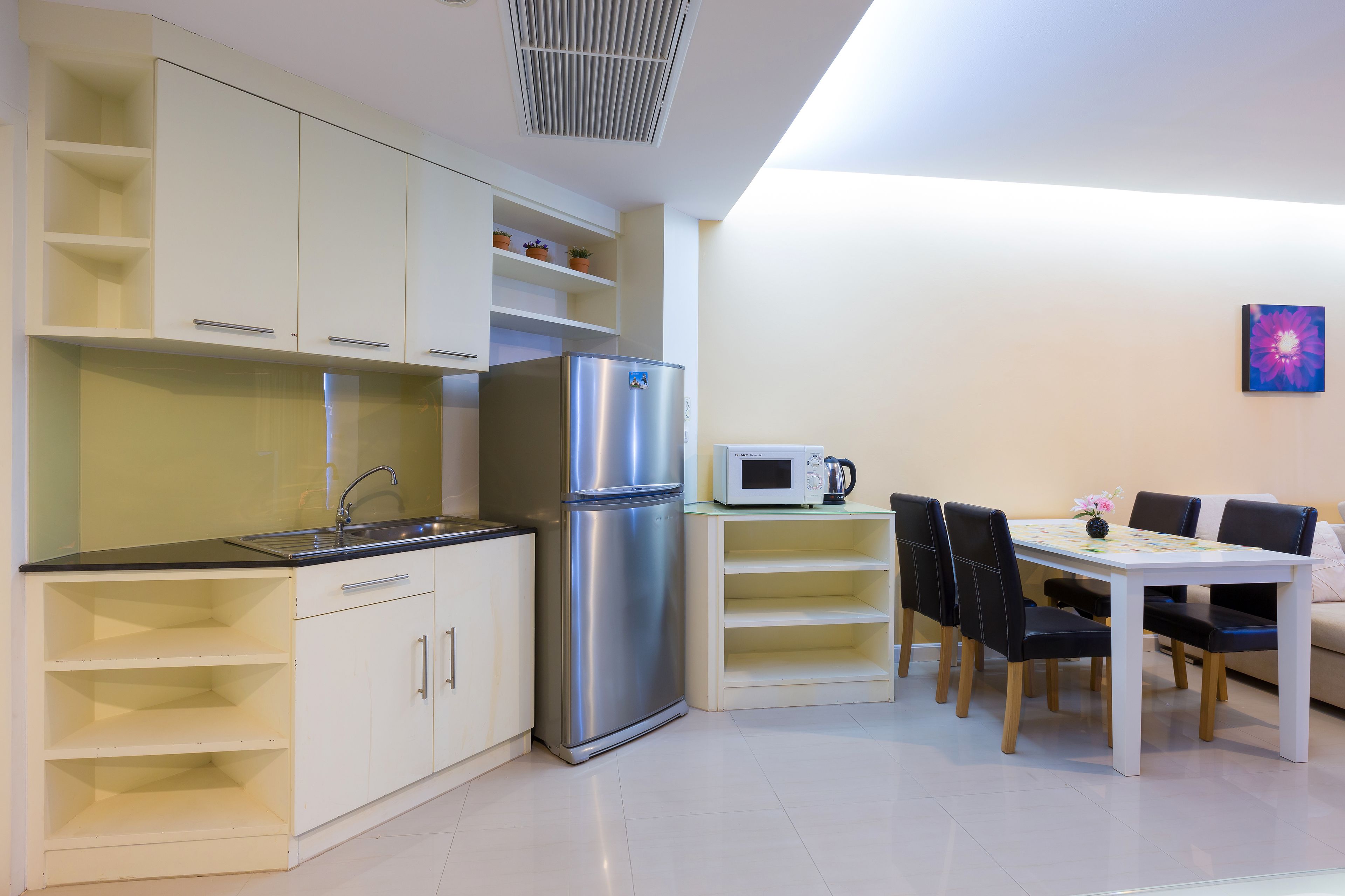 Cocina moderna con armarios blancos, un refrigerador de acero inoxidable, un microondas y un comedor con una mesa blanca y sillas negras.