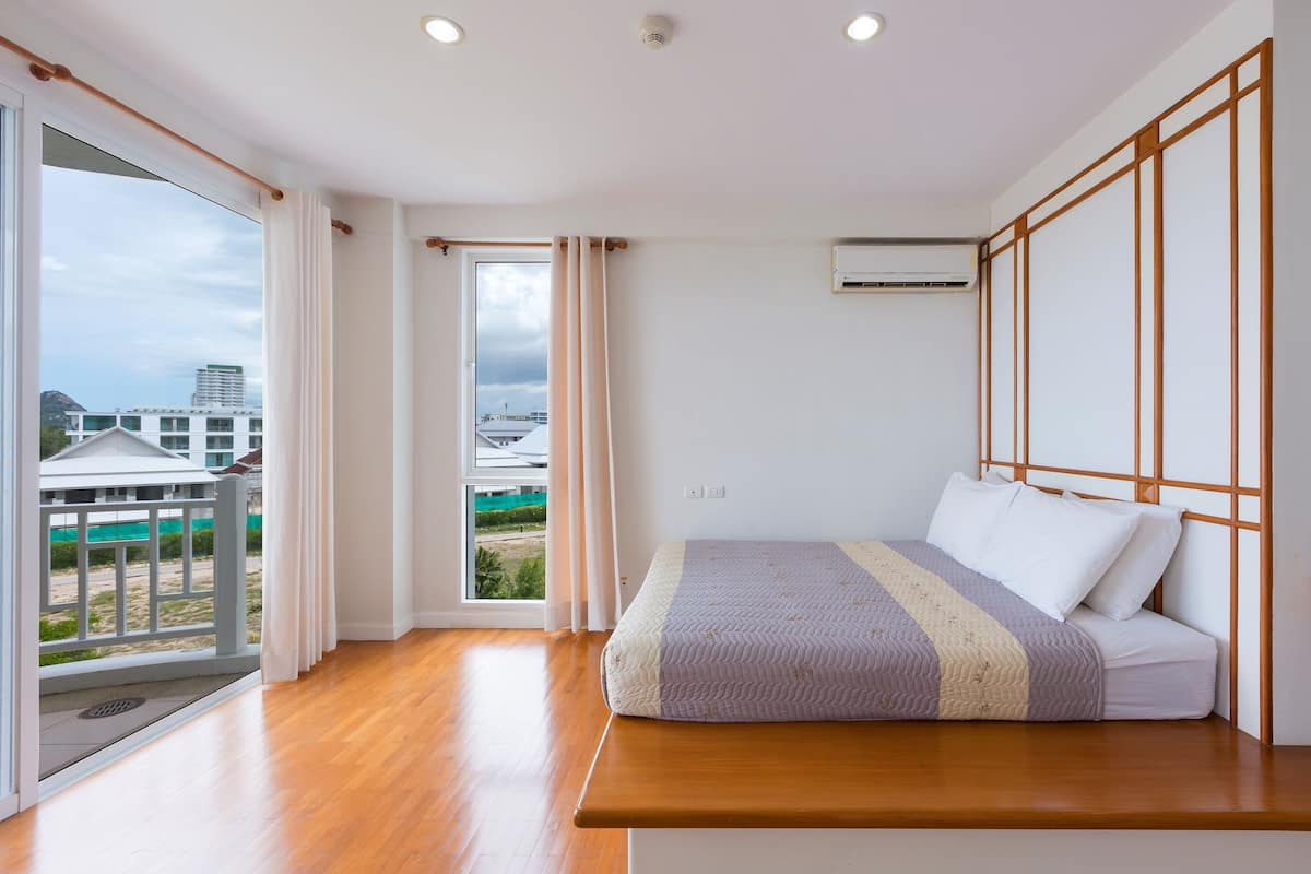 A bedroom with a wooden bed, a view of the outside, and an air conditioning unit.