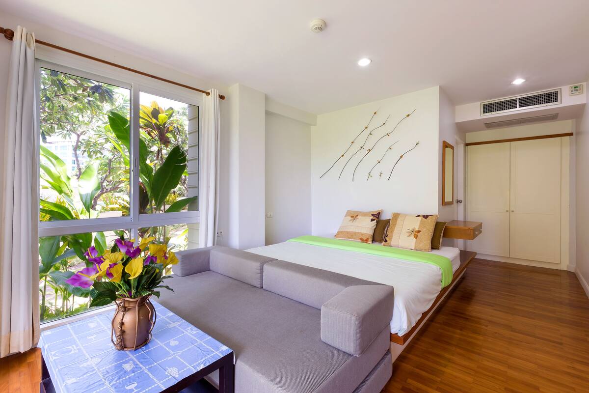 A bedroom with a bed, a sofa, a window with curtains, and a wall-mounted air conditioner.