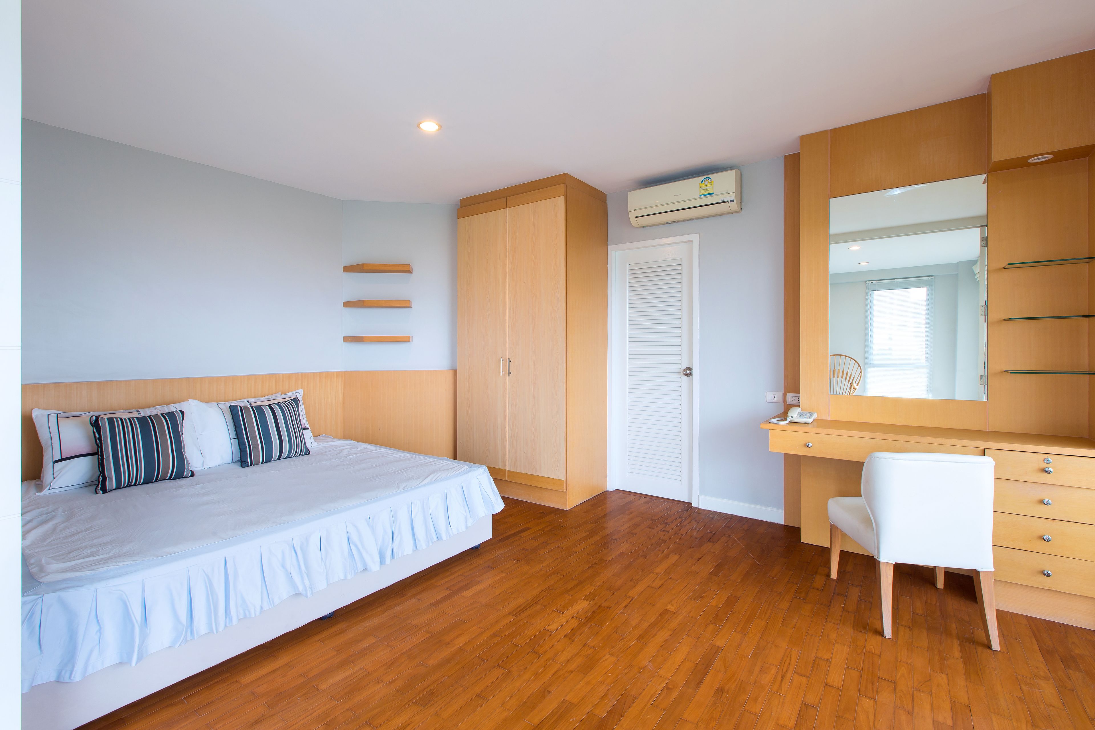 Un dormitorio con cama, escritorio, silla, armario y aire acondicionado.