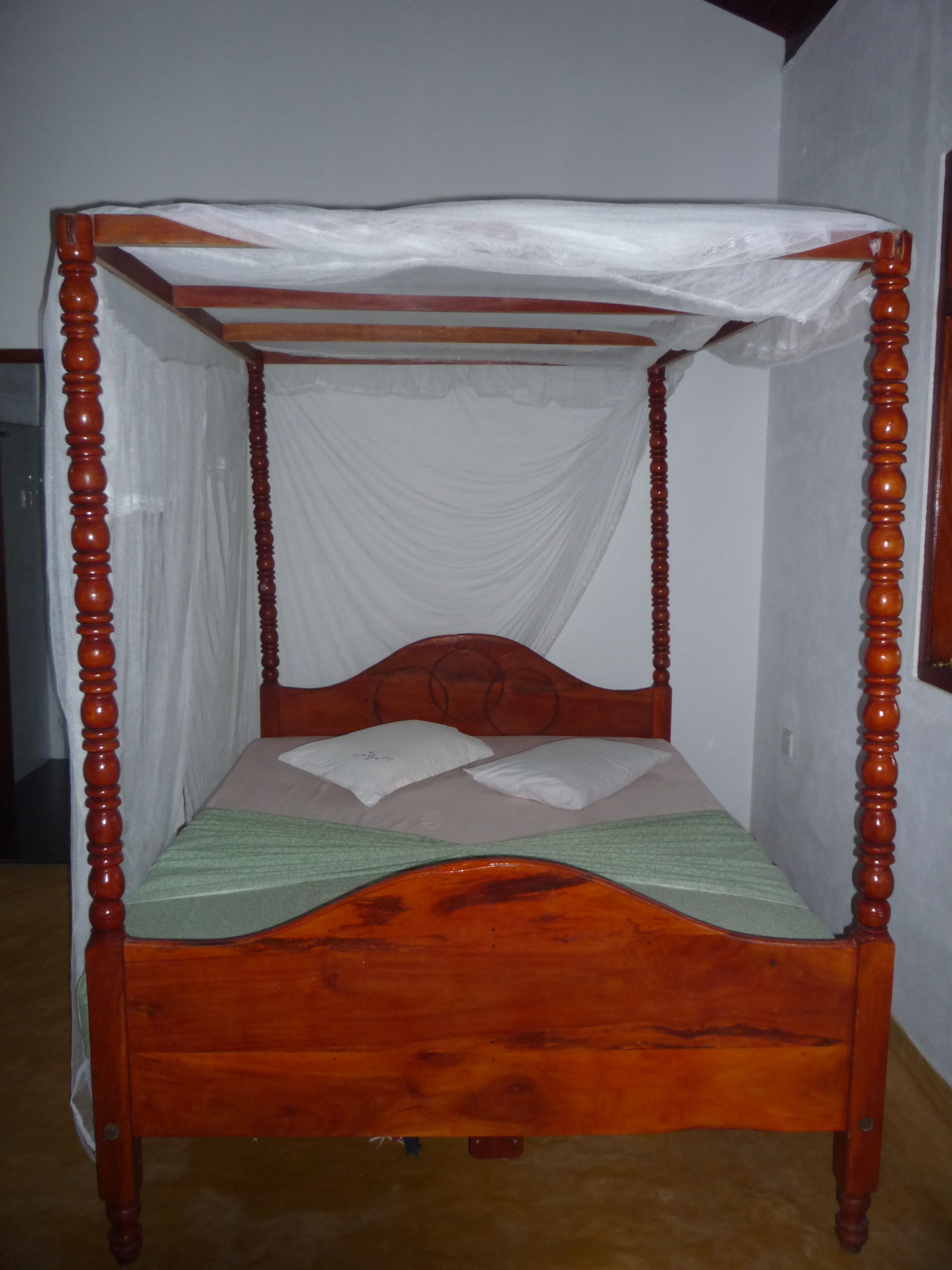 A wooden four-poster bed with a canopy, two pillows, and a green bedspread.
