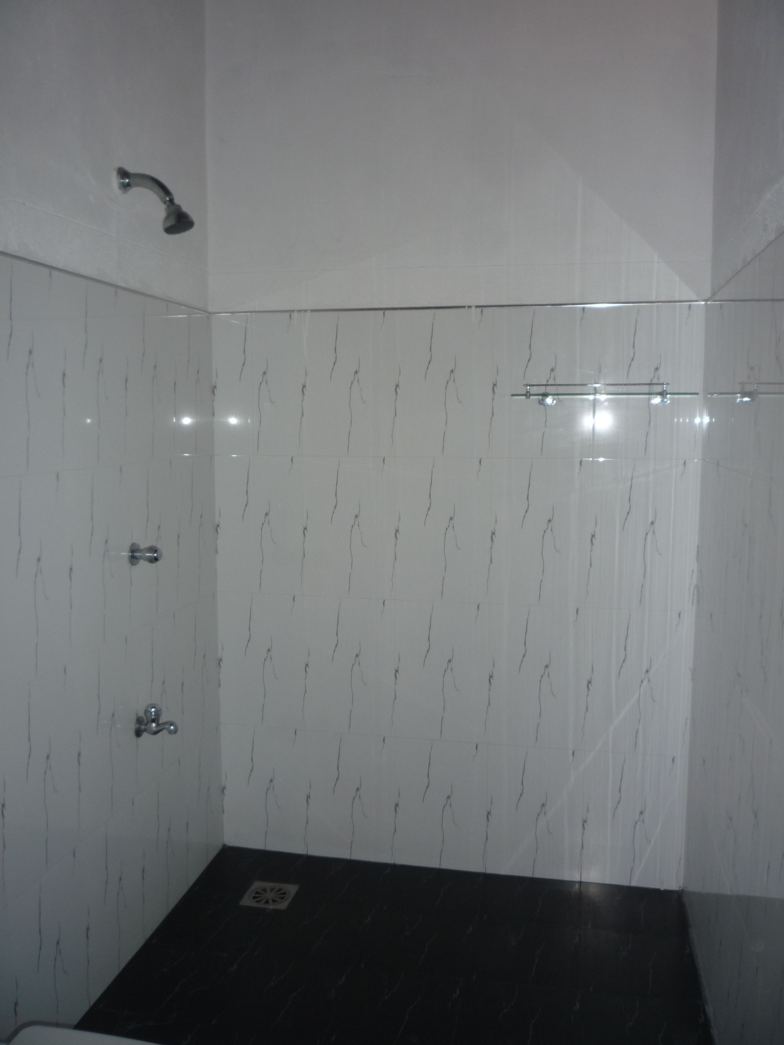 A bathroom with white marble walls, a black floor, and a glass shower enclosure.