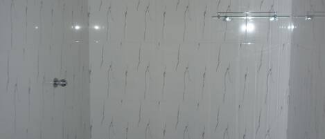 A bathroom with white marble walls, a black floor, and a glass shower enclosure.