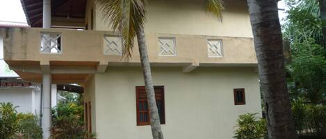 A two-story building with a flat roof, a balcony, and a small porch area.