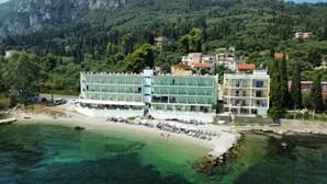 Ein Küstenhotel mit mehreren Etagen, einer Lage direkt am Strand und Blick auf die umliegenden bewaldeten Hügel.
