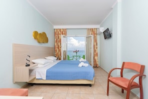 Habitación de hotel con una cama, una silla, un televisor y vista al mar.