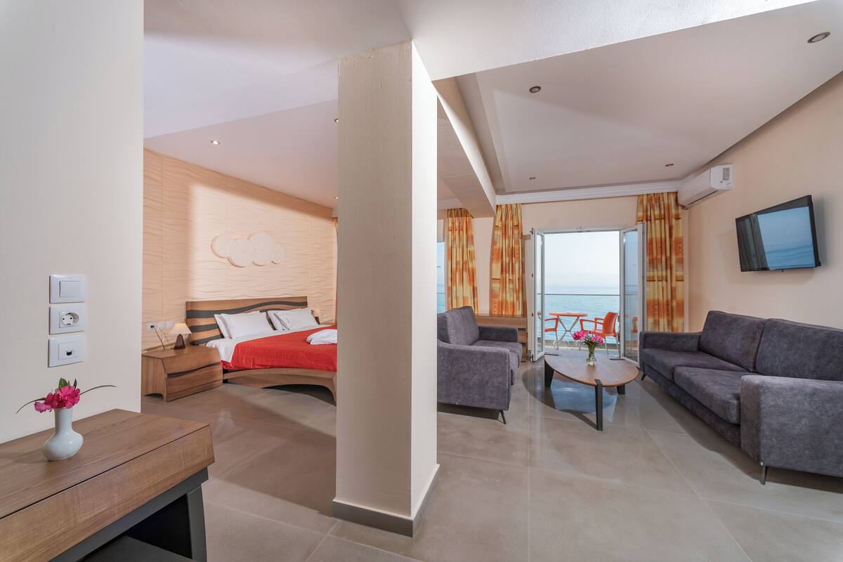 A modern hotel room with a bed, a sofa, a coffee table, and a TV.
