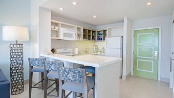 A modern kitchen with white appliances, a bar area with two chairs, and a green door.