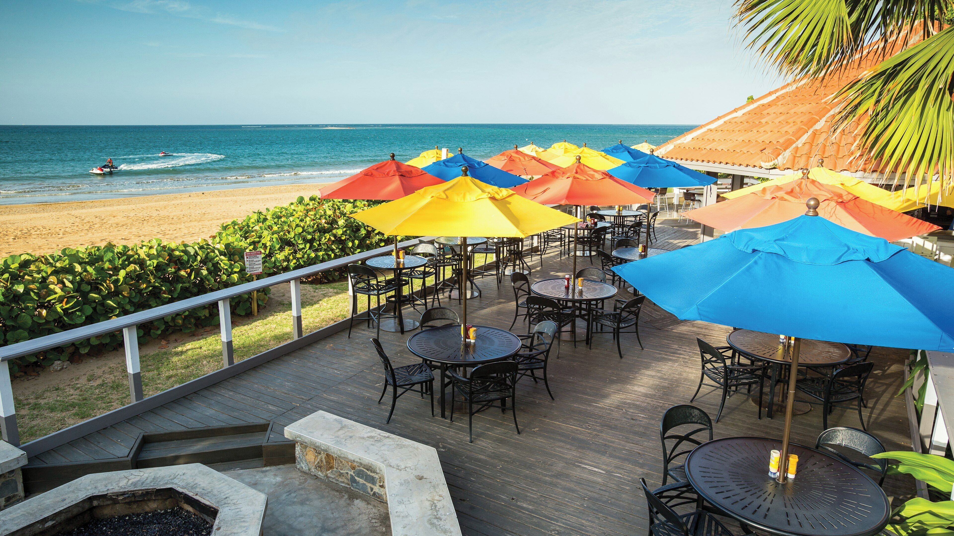 An outdoor seating area with tables and chairs, overlooking a beach and the ocean.