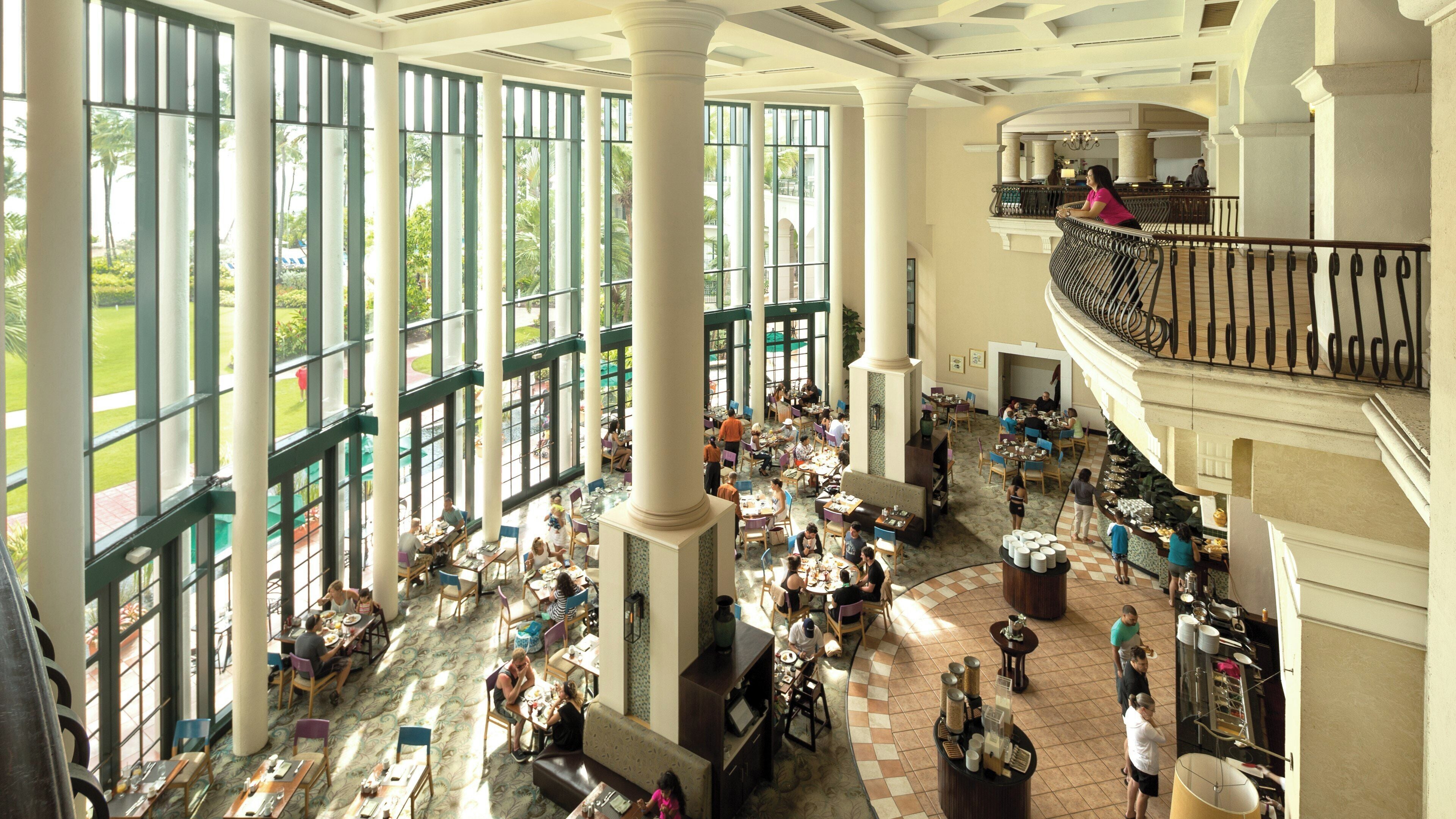 A spacious atrium with high ceilings and large windows, featuring multiple dining areas and a central open space.