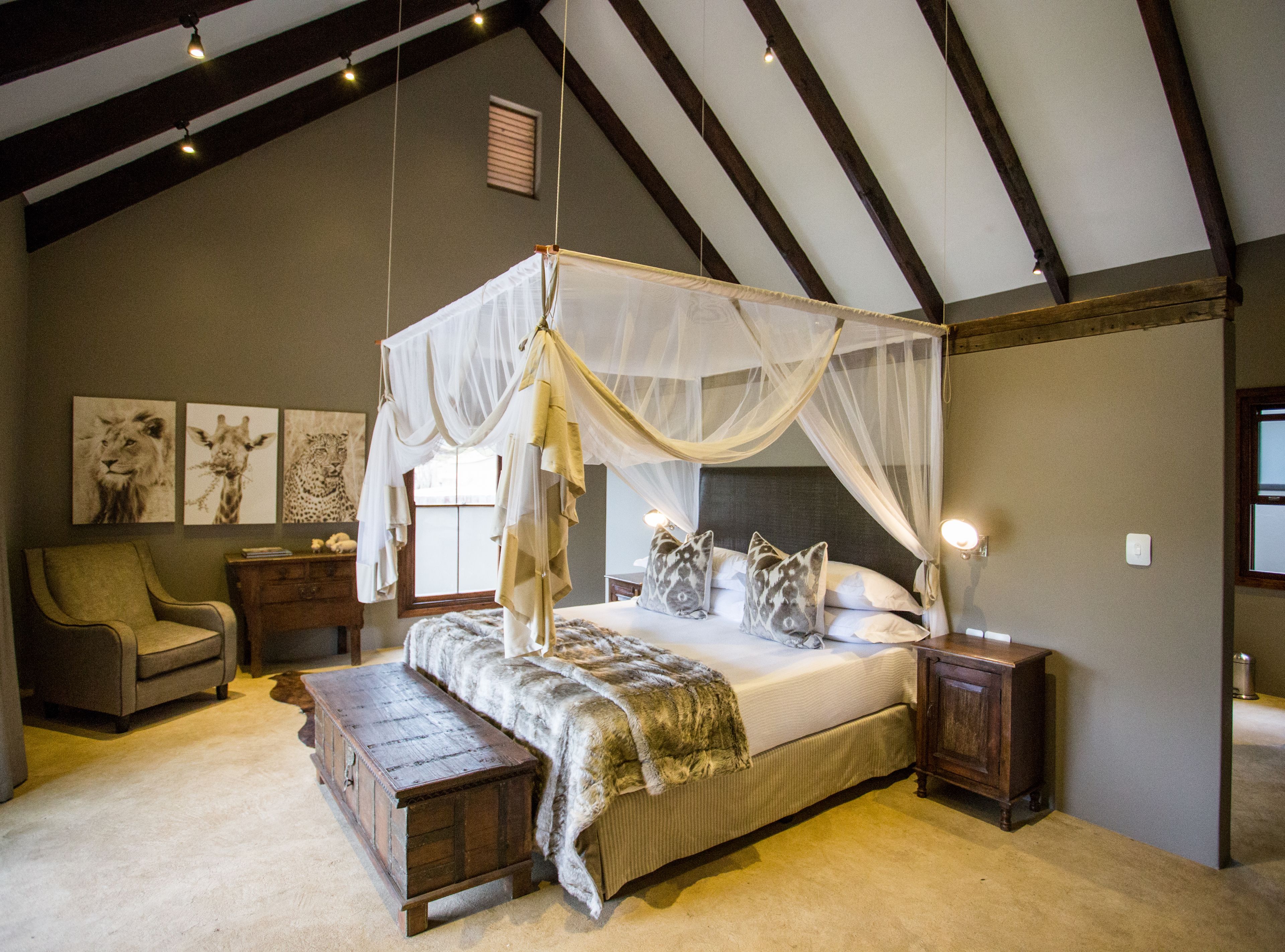 A bedroom with a four-poster canopy bed, a wooden bench, a nightstand, and a chair.