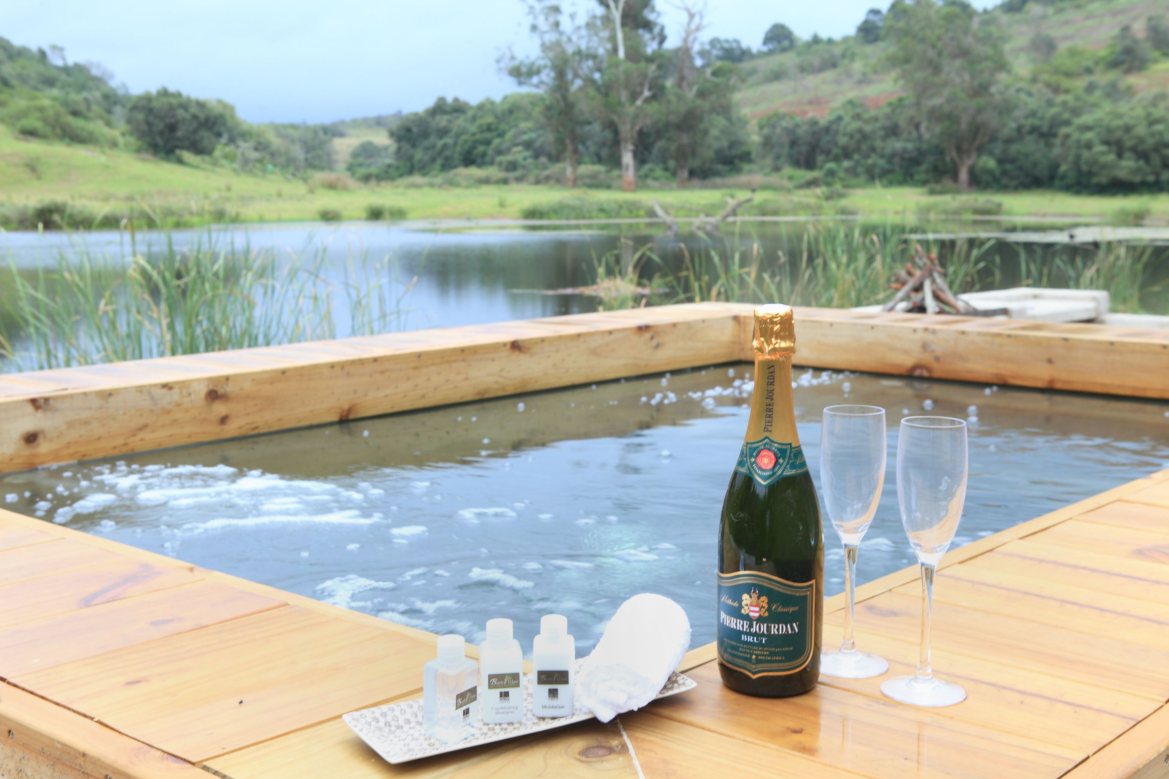 A wooden deck with a bottle of champagne, two glasses, and a tray of bottles.